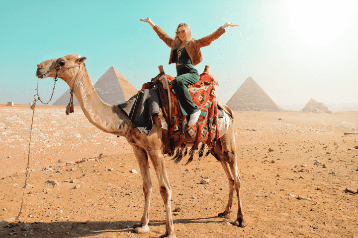 Person riding camel near pyramids in desert