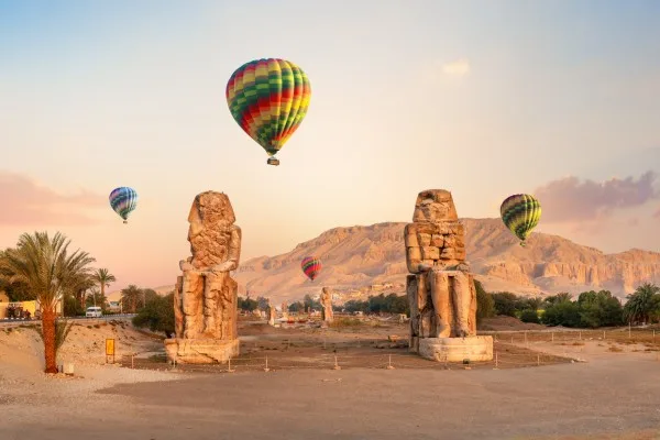Colorful hot air balloons over ancient statues.